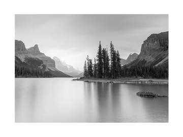 Schwarz-weiß-Fotografie eines ruhigen Sees mit einer kleinen Insel und hohen Bergen im Hintergrund.
