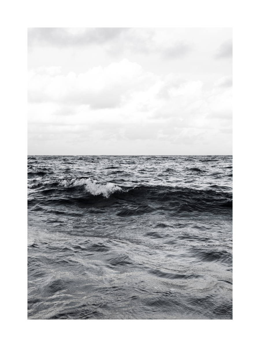 Fotografie einer Welle im Meer mit einem Berg im Hintergrund und einem rosa Himmel.