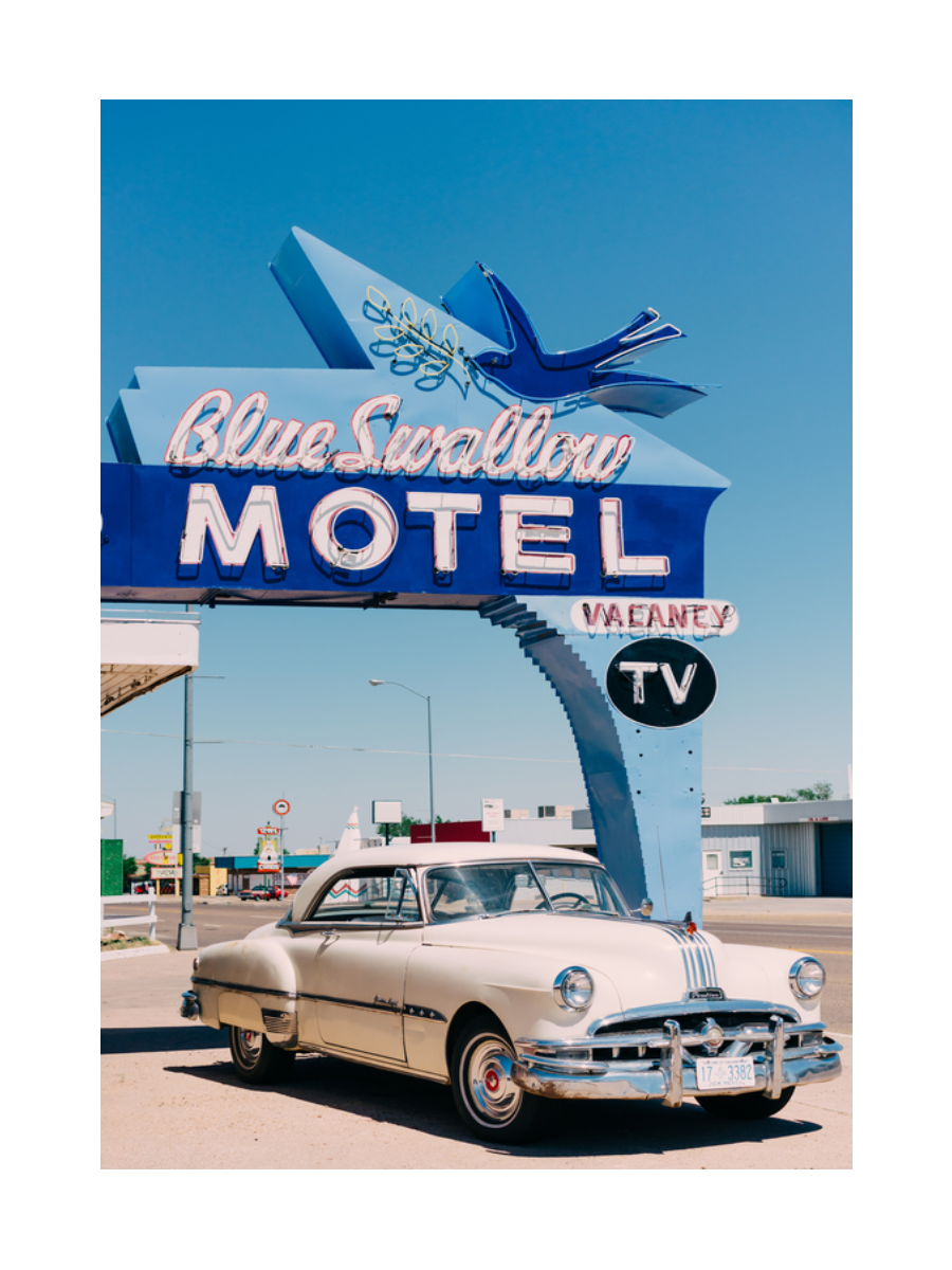 Fotografie eines klassischen Autos vor einem blauen Motel-Schild mit blauem Himmel.