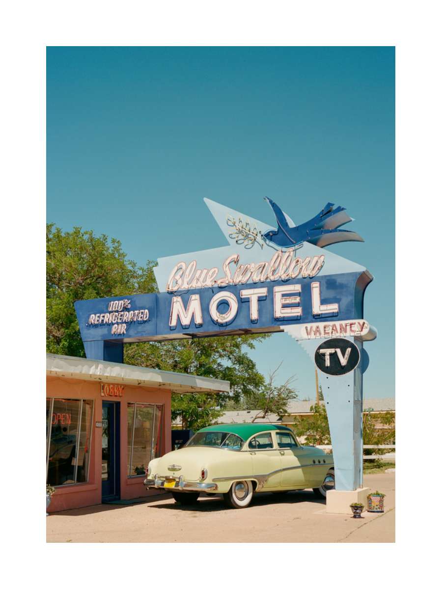 Fotografie des blauen „Blue Swallow Motel“-Schildes mit einem blauen Vogel und einem grünen Auto.