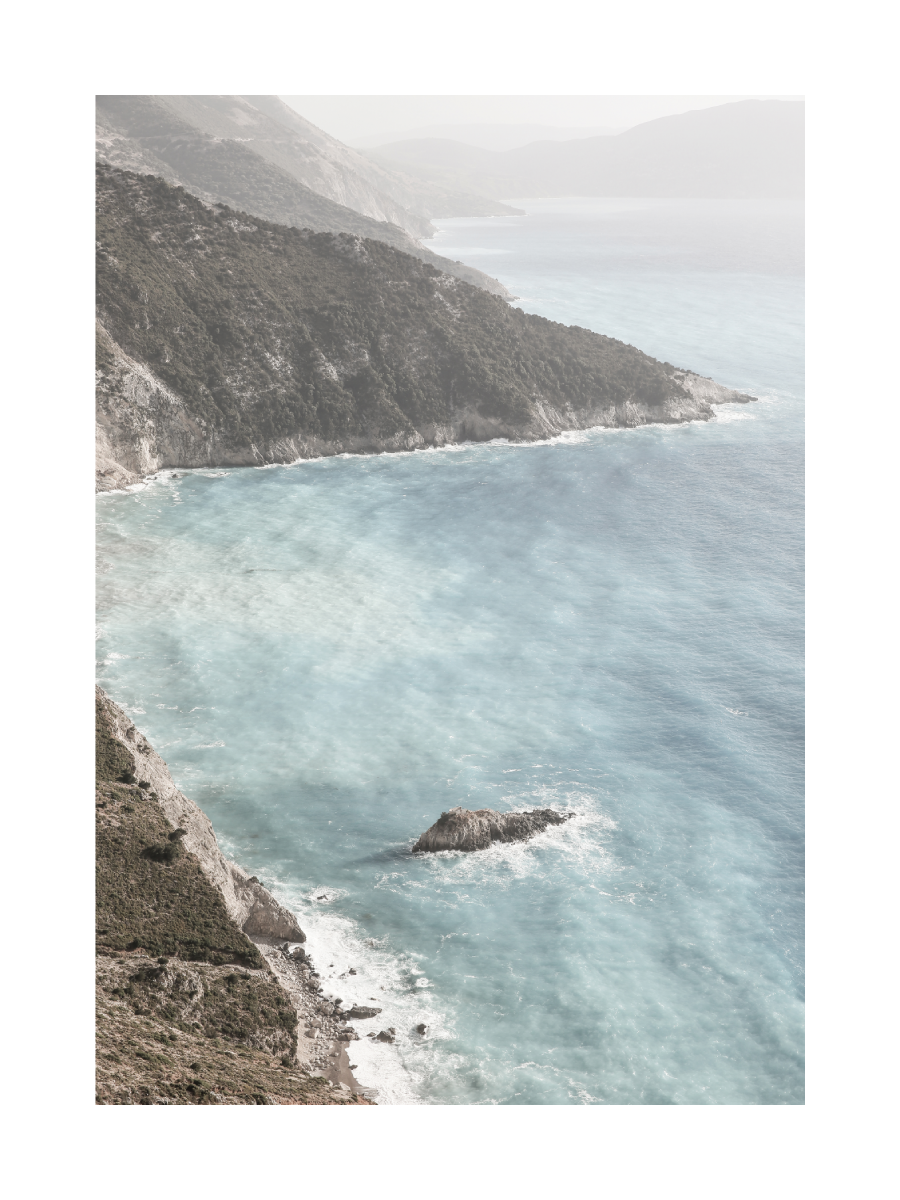 Fotografie von Klippen und blauem Wasser mit nebligem Himmel im Hintergrund.