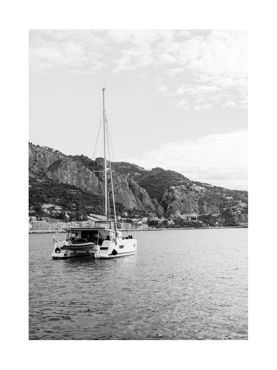 Schwarz-Weiß-Fotografie eines Bootes auf dem Wasser mit Bergen im Hintergrund.