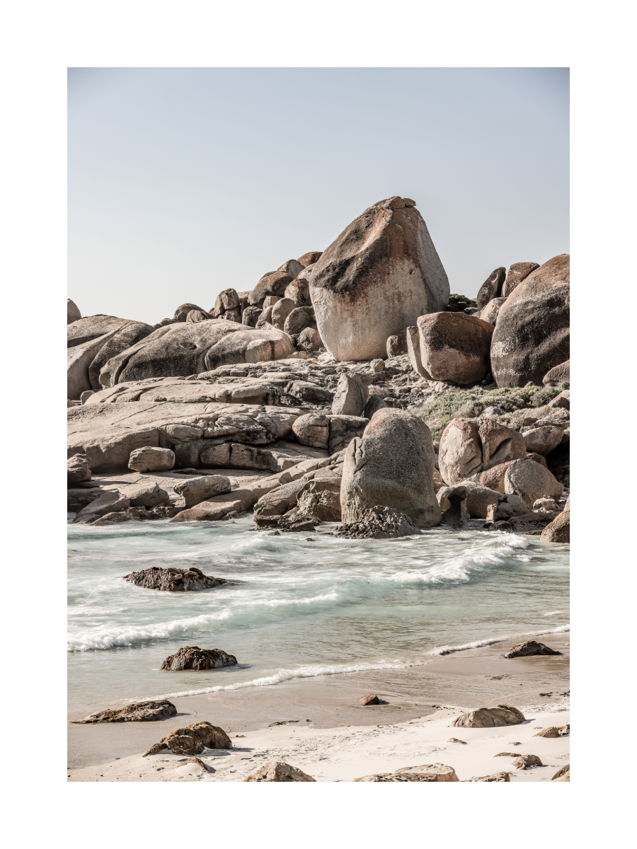 Fotografie von Felsen am Strand mit Wellen im Vordergrund.