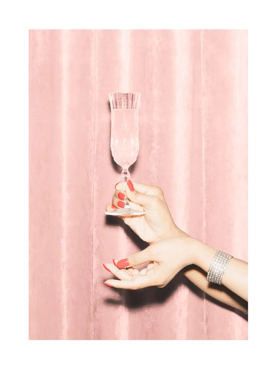 Hand mit roten Nägeln hält ein Champagnerglas vor rosa Hintergrund.