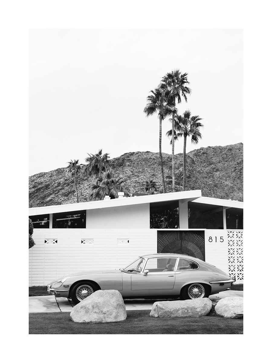 Schwarz-weiß-Fotografie eines klassischen Autos vor einem weißen Haus mit Palmen im Hintergrund.