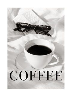 Eine Tasse Kaffee auf einem Bett mit einer Sonnenbrille und einem Buch daneben.