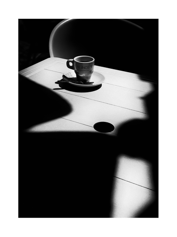 Schwarz-Weiß-Fotografie einer Kaffeetasse auf einem Tisch mit Schatten.