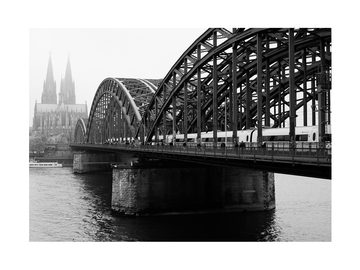 Schwarz-weiß-Fotografie der Hohenzollernbrücke in Köln mit dem Kölner Dom im Hintergrund.
