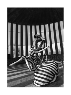 Schwarz-weiß-Fotografie einer Ballerina in einem gestreiften Kleid, die in einem großen, runden Raum tanzt.