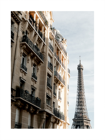 Fotografie eines Pariser Gebäudes mit dem Eiffelturm im Hintergrund und blauem Himmel.