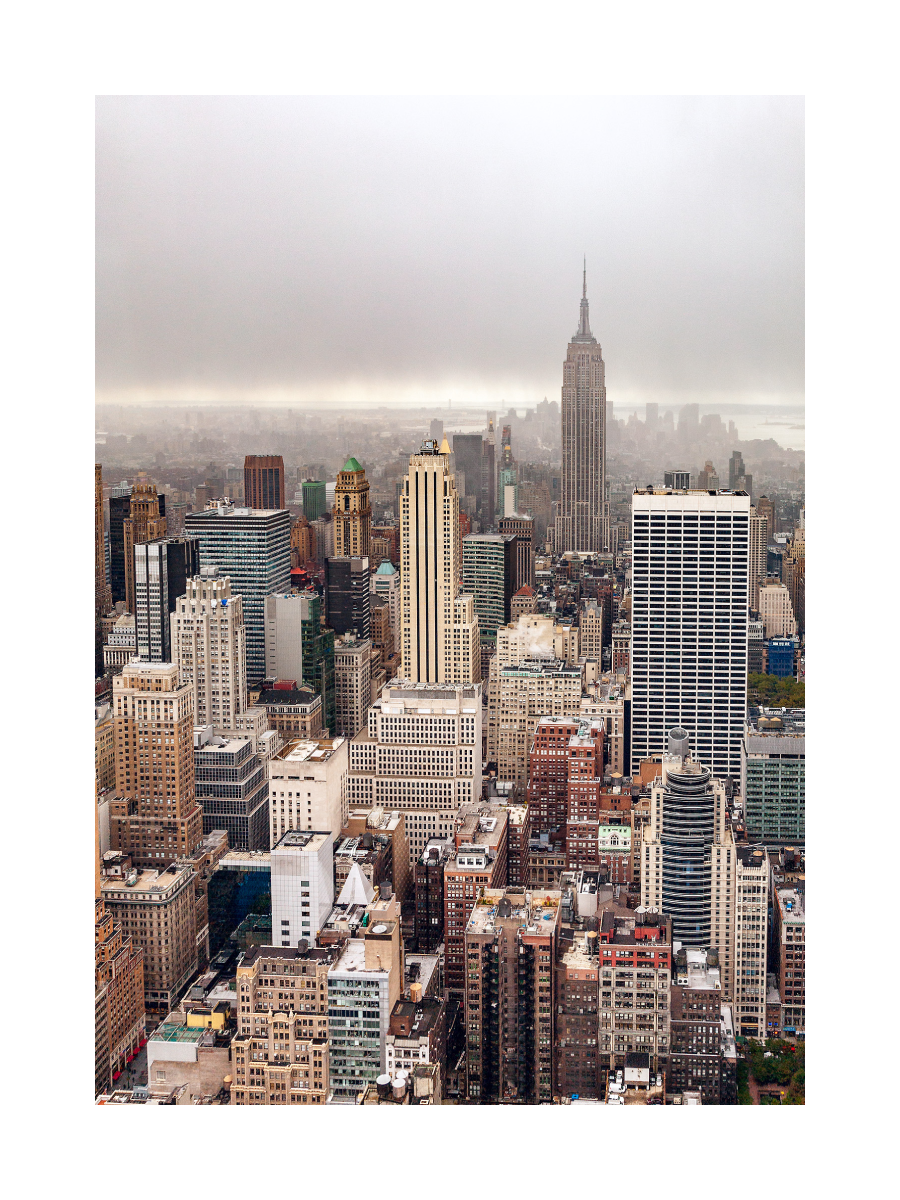 Fotografie von New York City mit dem Empire State Building und Wolkenkratzern vor einem grauen Himmel.