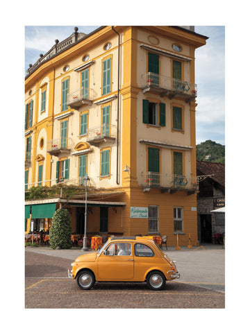 Ein gelbes Vintage-Auto vor einem gelben Gebäude mit grünen Fensterläden.