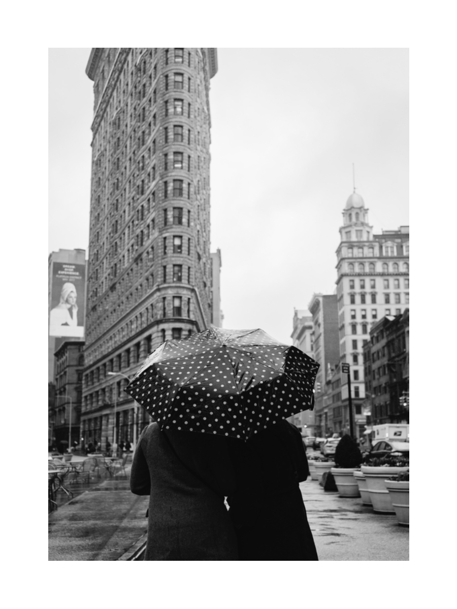 Ein Paar unter einem gepunkteten Regenschirm vor dem Flatiron Building in New York.