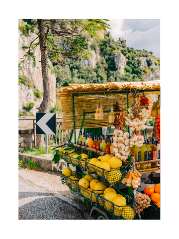 Obst- und Getränkestand am Straßenrand auf der Amalfiküste mit Zitronen, Knoblauch und Getränkeflaschen.