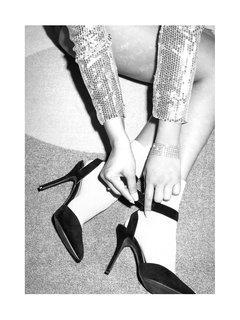 Schwarz-weiß-Fotografie einer Person mit weißen Socken und schwarzen High Heels, Pailletten-Kleid und Armband.