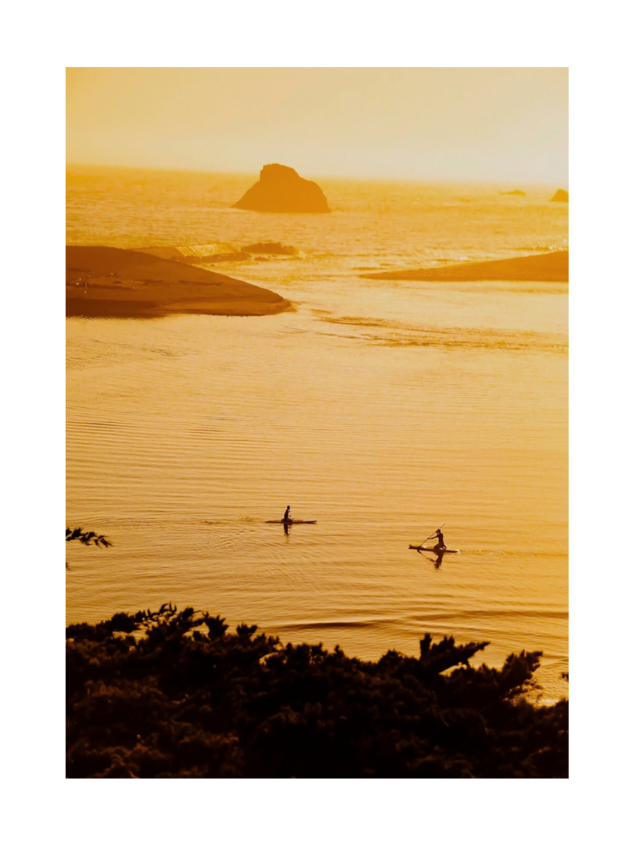 Fotografie von zwei Personen beim Stand-up-Paddling unter einem orangefarbenen Himmel.