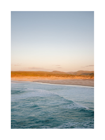 Fotografie eines Strandes mit türkisfarbenem Wasser und goldenem Sonnenuntergang.