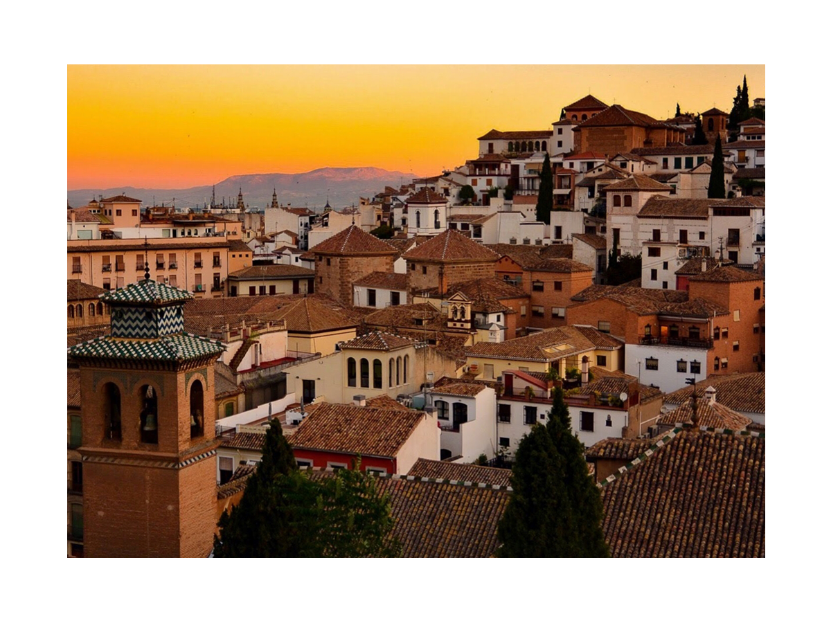 Sonnenuntergang über der Stadt Granada mit traditionellen Gebäuden und einem orangefarbenen Himmel.