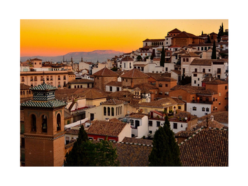 Sonnenuntergang über der Stadt Granada mit traditionellen Gebäuden und einem orangefarbenen Himmel.