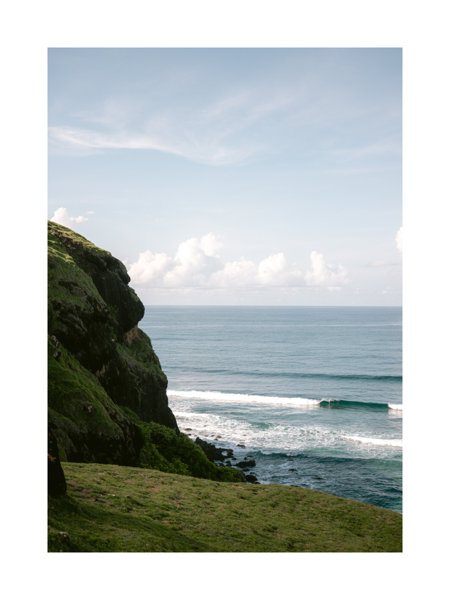 Fotografie einer grünen Klippe am Meer mit blauem Himmel und Wolken.