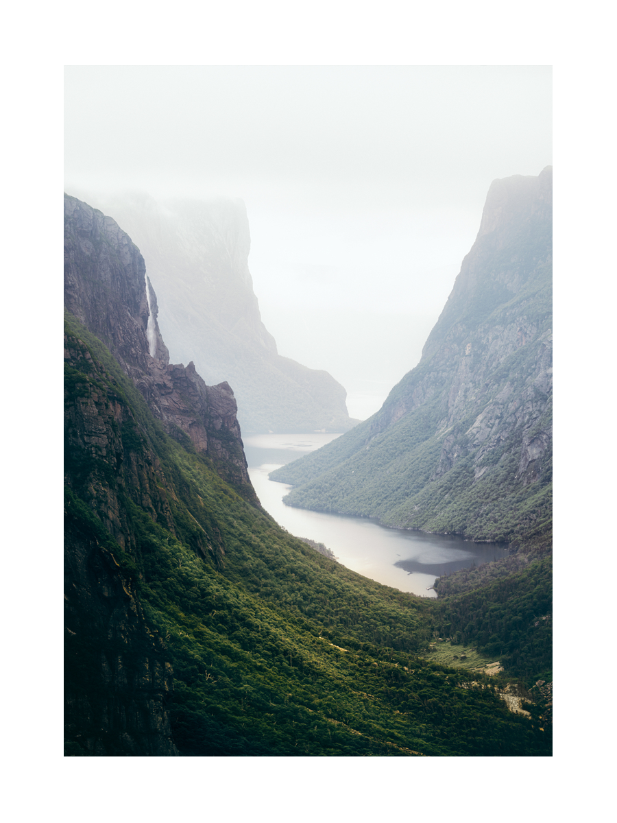 Fotografie eines grünen Tals mit Fluss und nebelverhangenen Bergen.