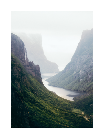 Fotografie eines grünen Tals mit Fluss und nebelverhangenen Bergen.