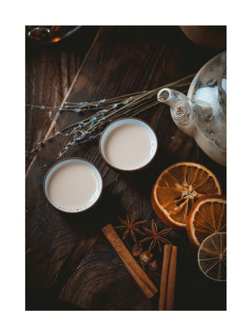 Zwei Tassen Chai-Tee mit getrockneten Orangenscheiben und Zimtstangen auf rustikalem Holzuntergrund.