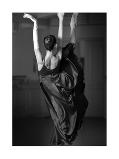Schwarz-Weiß-Fotografie einer Ballerina in einem schwarzen Kleid, die in einem Tanzstudio tanzt.