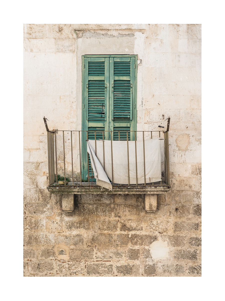Fotografie eines kleinen Balkons mit grünen Fensterläden und einem weißen Tuch über dem Geländer.