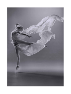 Schwarz-Weiß-Fotografie einer Ballerina in einem fließenden weißen Kleid in Bewegung.