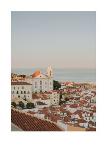 Blick auf Lissabon mit roten Dächern und einer Kirche im Vordergrund, Meer im Hintergrund.