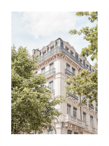 Fotografie eines großen, alten Gebäudes mit Balkonen und vielen Fenstern, umgeben von grünen Bäumen.