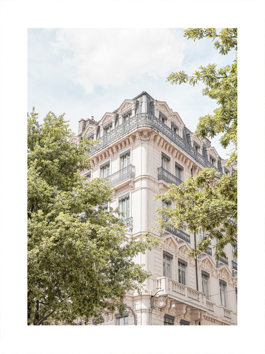 Fotografie eines großen, alten Gebäudes mit Balkonen und vielen Fenstern, umgeben von grünen Bäumen.