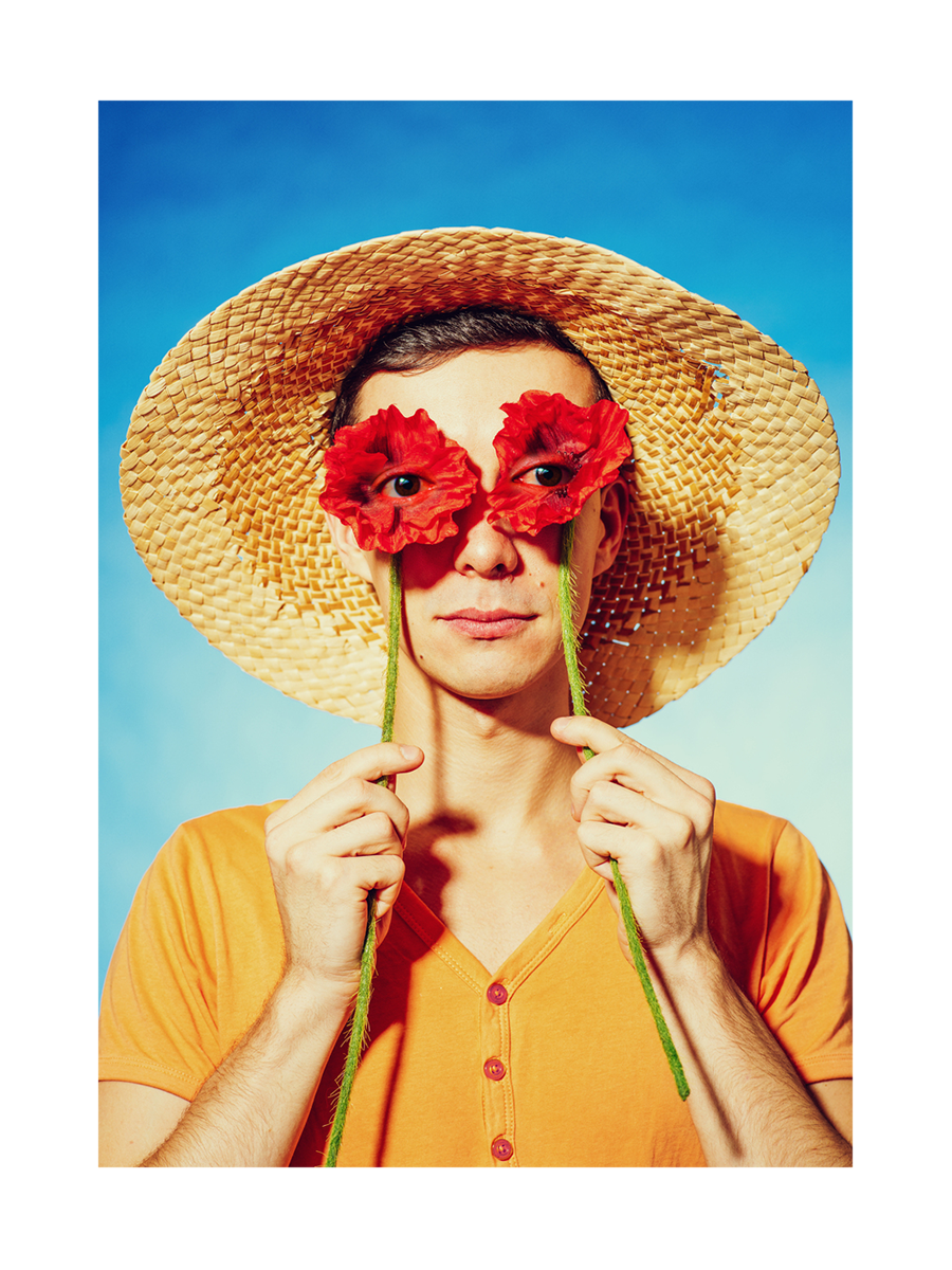 Mann mit Strohhut und roten Blumen vor den Augen vor blauem Himmel.