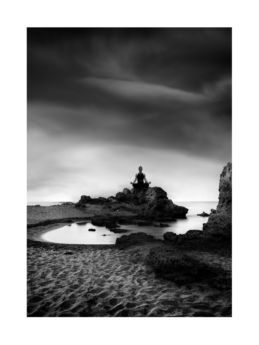 Person meditiert auf einem Felsen am Strand in monochromer Farbgebung.