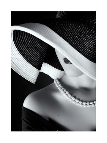 Schwarz-weiß-Fotografie einer Frau mit breitrandigem Hut und Perlenkette.