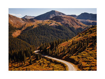 Fotografie einer kurvenreichen Straße in einer herbstlichen Berglandschaft mit blauem Himmel.