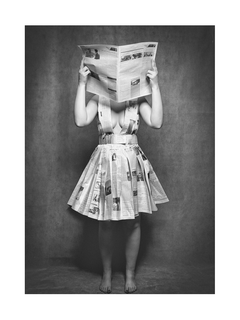 Schwarz-weiß-Fotografie einer Frau in einem Kleid aus Zeitungspapier, die eine Zeitung liest.