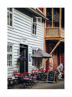Fotografie eines norwegischen Cafés mit roten Stühlen und grauem Sonnenschirm vor einem weißen Gebäude.