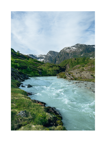 Ein Fluss in Norwegen, umgeben von grüner Landschaft und schneebedeckten Bergen unter blauem Himmel.