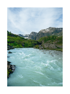 Ein Fluss fließt durch eine grüne Landschaft mit schneebedeckten Bergen im Hintergrund.