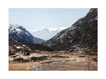 Fotografie einer rotbraunen Hütte in einem Tal mit schneebedeckten Bergen im Hintergrund.