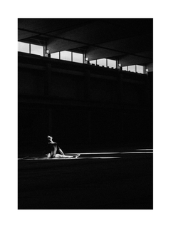 Schwarz-Weiß-Fotografie einer nackten Frau, die in einem dunklen Raum im Licht sitzt.