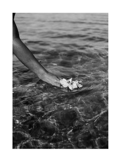 Schwarz-Weiß-Fotografie einer Hand, die weiße Blumen auf das Wasser legt.