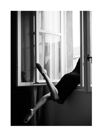 Schwarz-Weiß-Fotografie einer Frau, die in einem Fenster sitzt, mit dem Kopf draußen und den Beinen drinnen.
