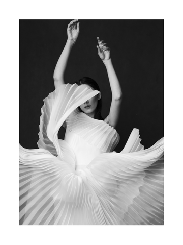 Schwarzweiß-Fotografie einer Frau in einem weißen, plissierten Kleid.