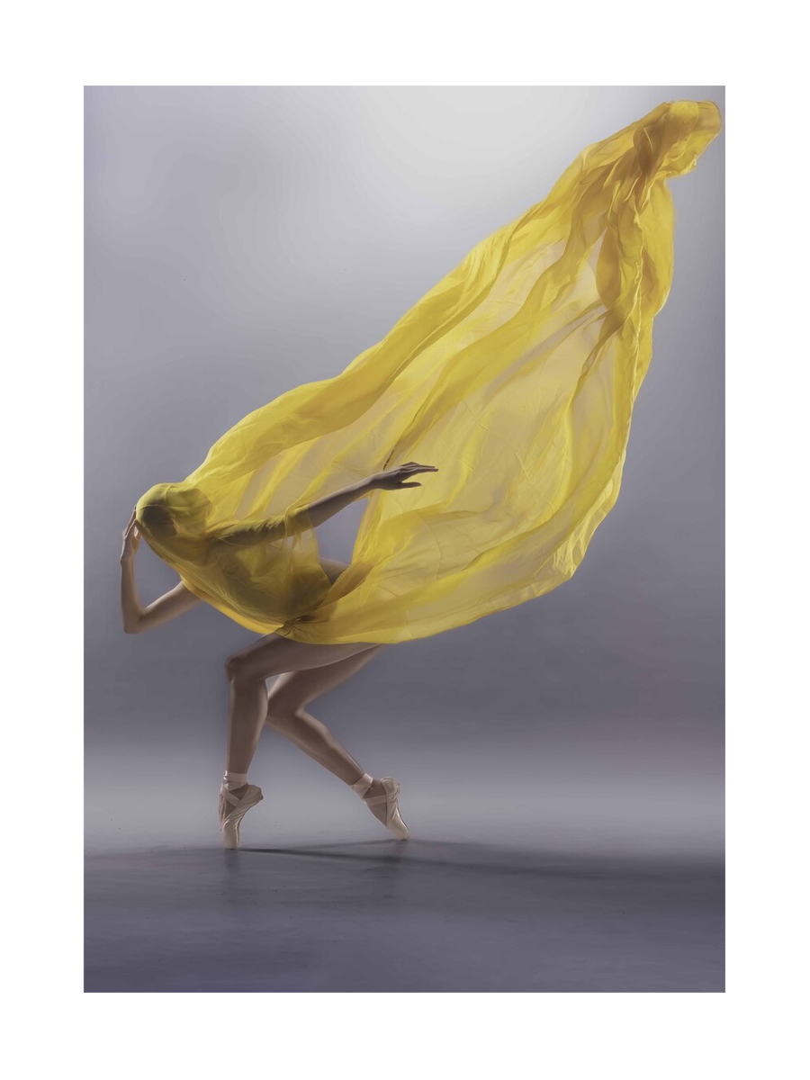 Ballerina in einem gelben Kleid auf Zehenspitzen vor grauem Hintergrund.