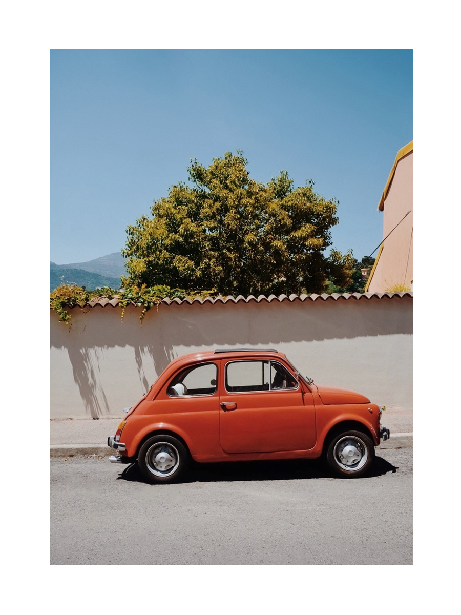 Fotografie eines roten Autos vor einer Mauer mit einem Baum im Hintergrund.
