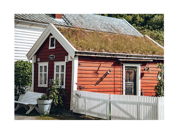 Ein rotes Haus mit grasbewachsenem Dach und weißem Zaun, umgeben von Pflanzen.