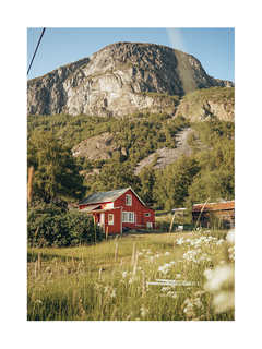 Ein rotes Haus in der Natur, umgeben von grünen Bäumen und Bergen.
